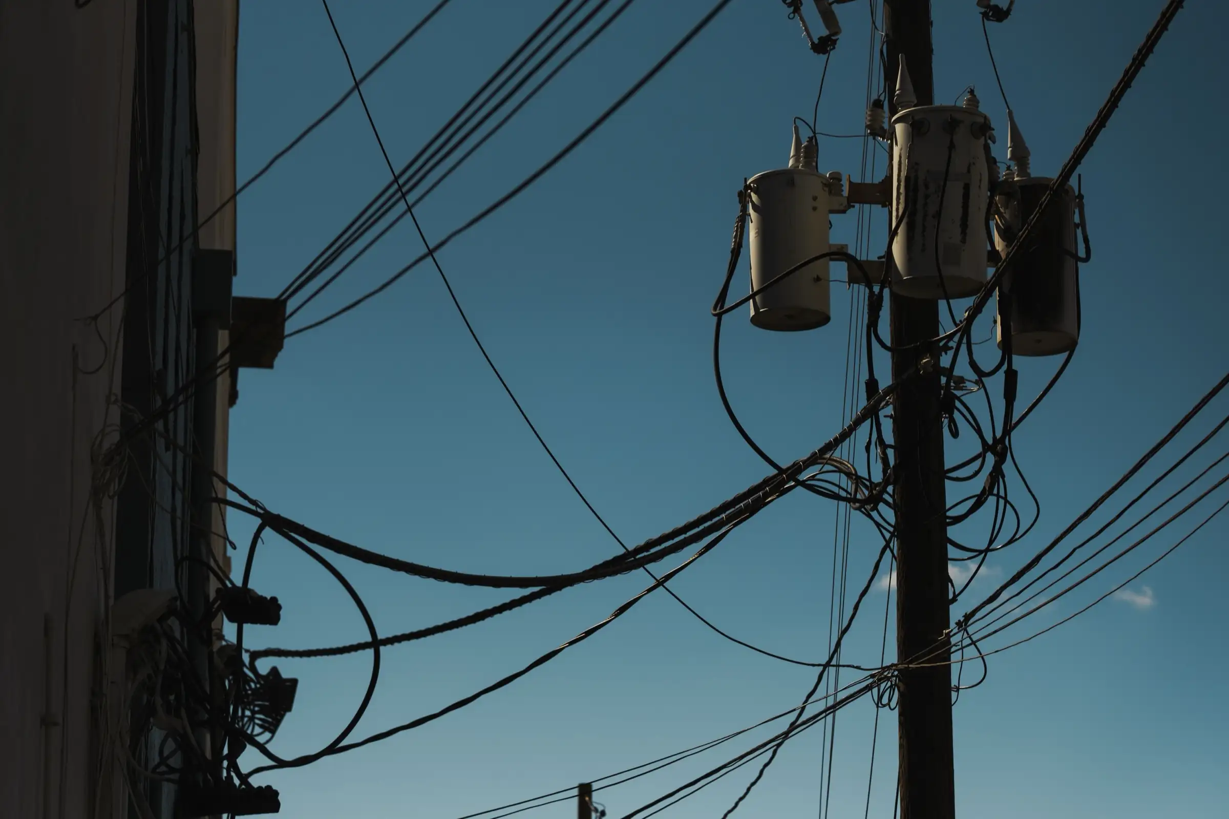 Pole-mounted transformers and overhead distribution wiring against a clear sky
