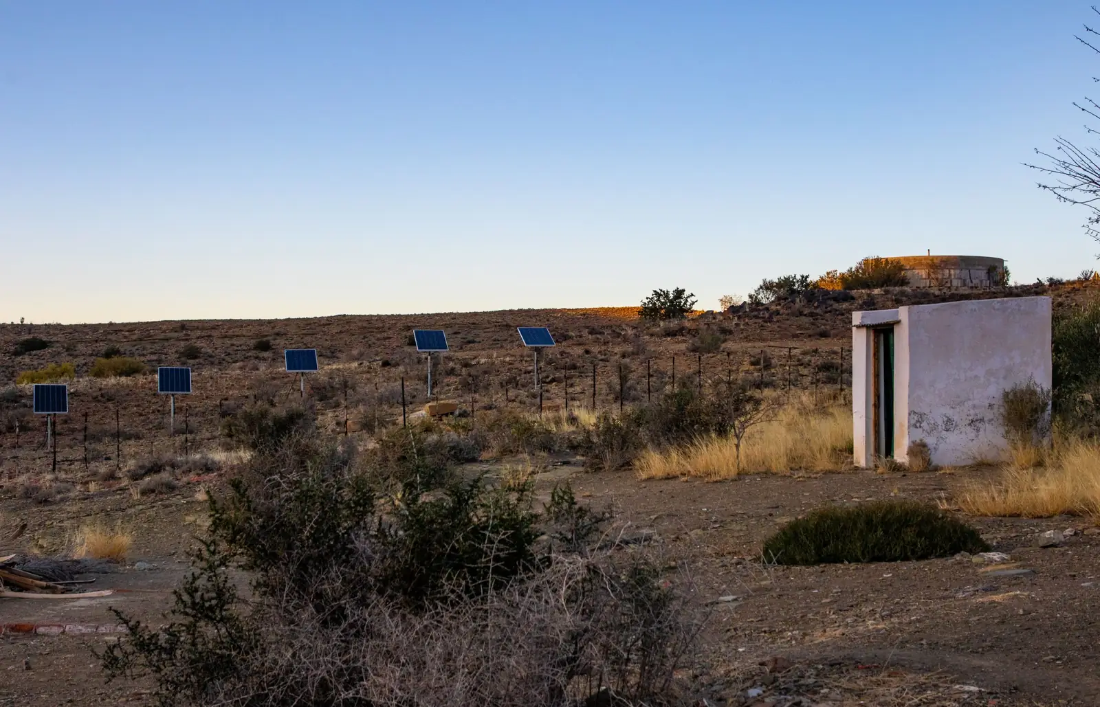 Pole-mounted solar panels beside a pump house in arid scrubland
