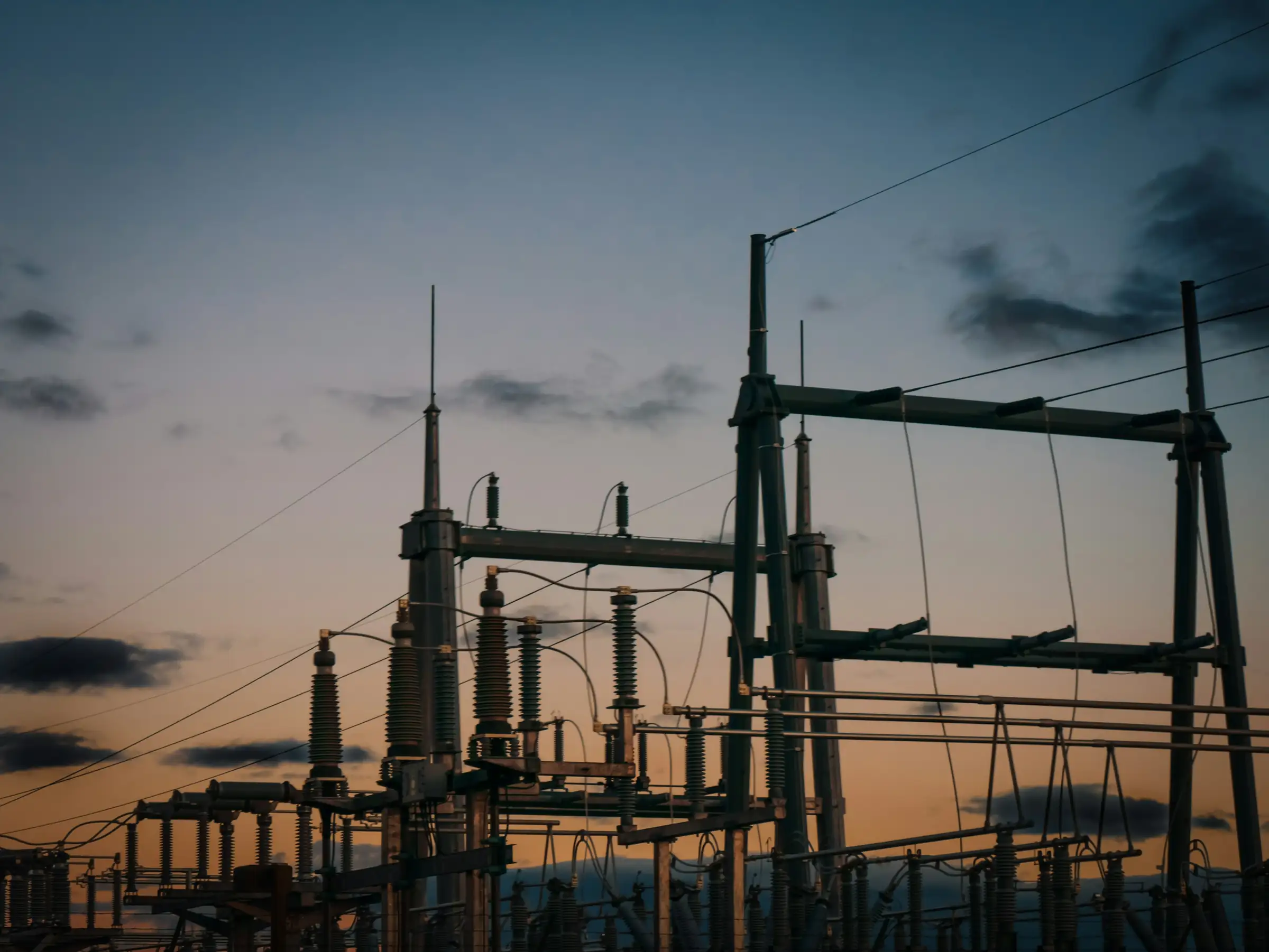 High voltage substation structures silhouetted against a dusk sky